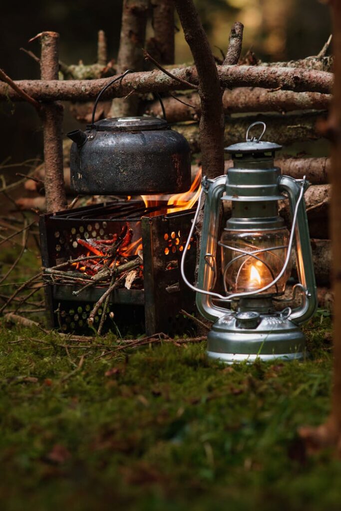 Rustic outdoor campfire setting with a kettle and a glowing lantern on mossy ground.